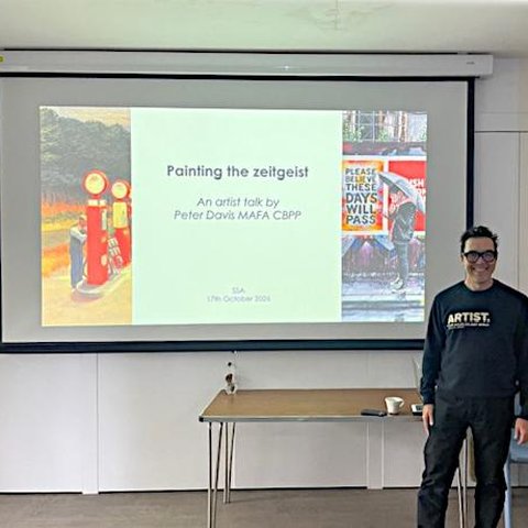 Artist Peter Davis is seen standing infrom of a projection screen - Talk Title "Painting The Zeitgeist".